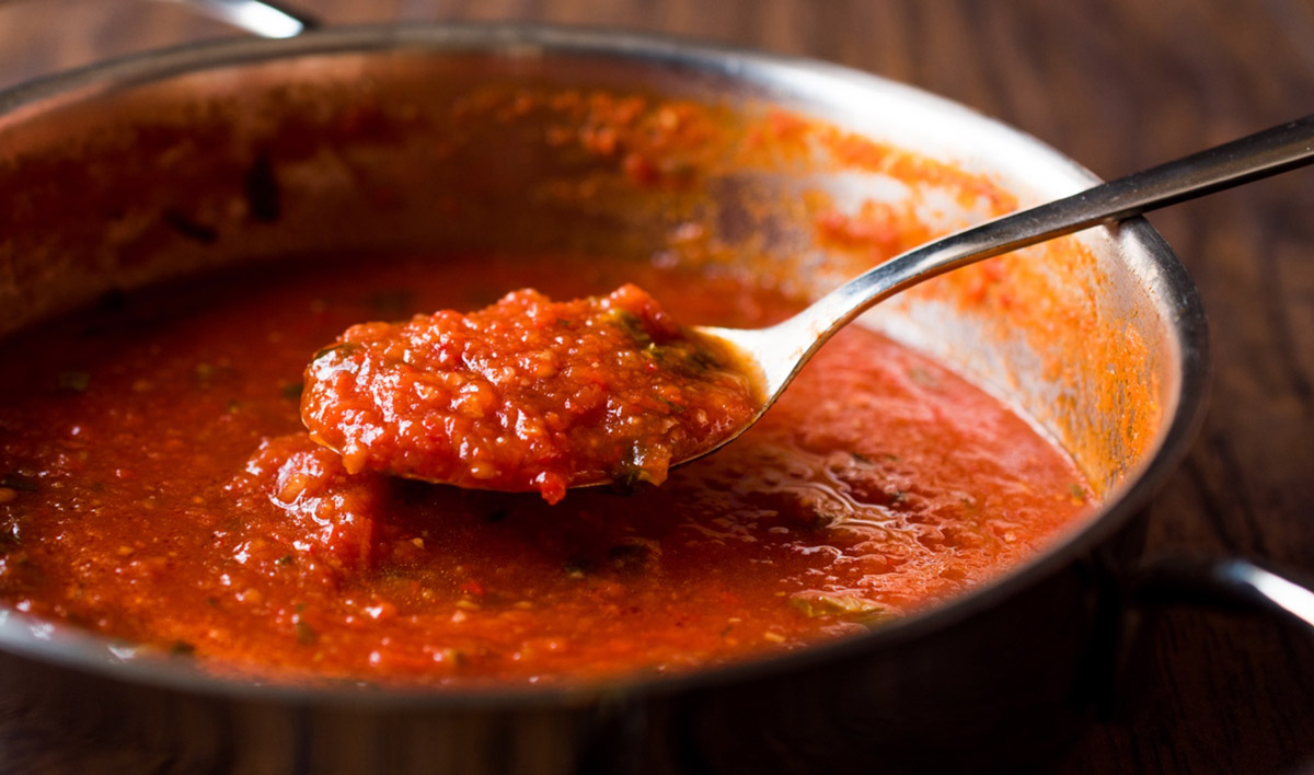 Pot of cooked tomato sauce with spoon showing thickness