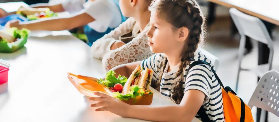 Elementary school girl enjoying a nutritious packed lunch in the cafeteria.