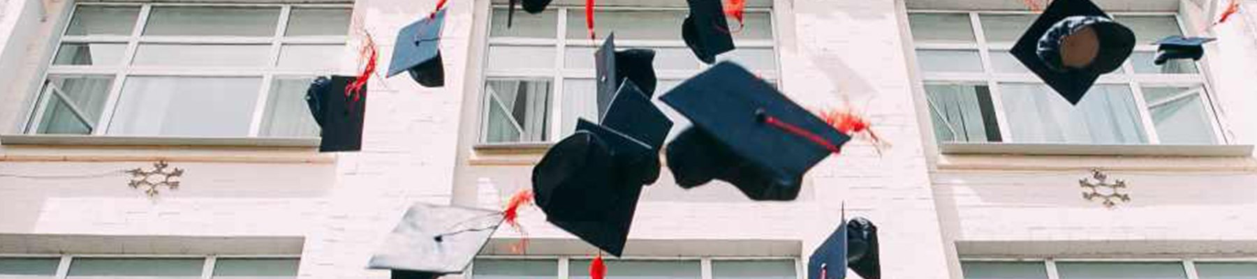 Graduation caps thrown into the air in celebration outside a school building.